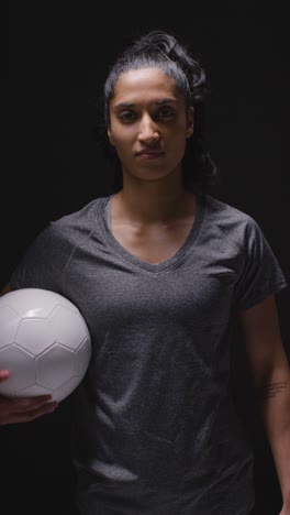 Vertikales-Videostudioporträt-Einer-Fußballspielerin-In-Sportkleidung,-Die-Den-Ball-Hält